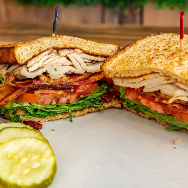 A Buttermilk Eatery club sandwich, cut in half, with turkey, bacon, lettuce, tomato, and pickles.
