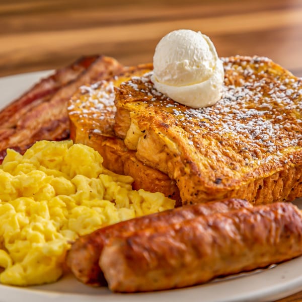 Buttermilk Eatery's French toast with powdered sugar, a scoop of butter, scrambled eggs, bacon, and sausage.