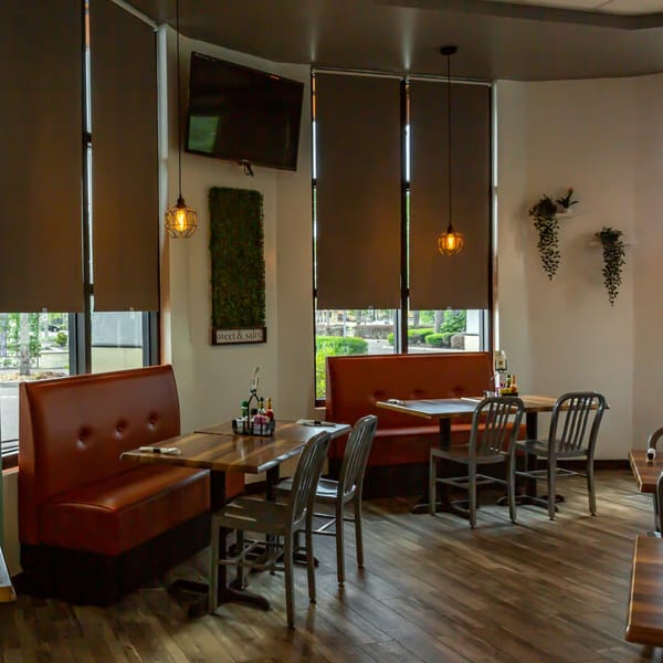 Buttermilk Eatery's dining room features brown booths, wooden tables, metal chairs, and large windows with shades.