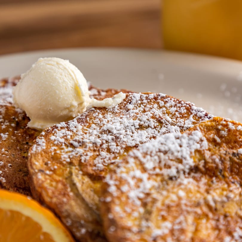 Buttermilk Eatery's French toast, powdered sugar, butter, and an orange slice on a white plate.