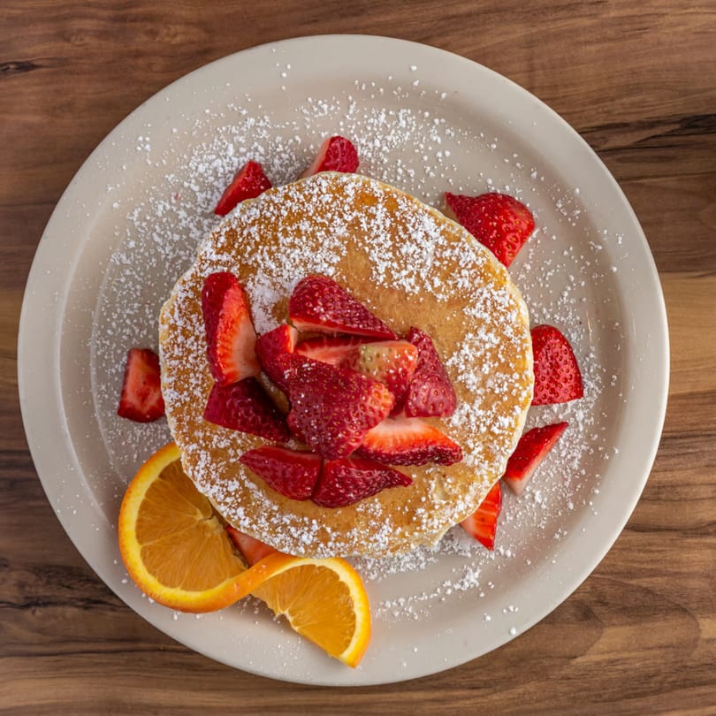 Buttermilk Eatery's pancakes topped with fresh strawberries, powdered sugar, and an orange slice.