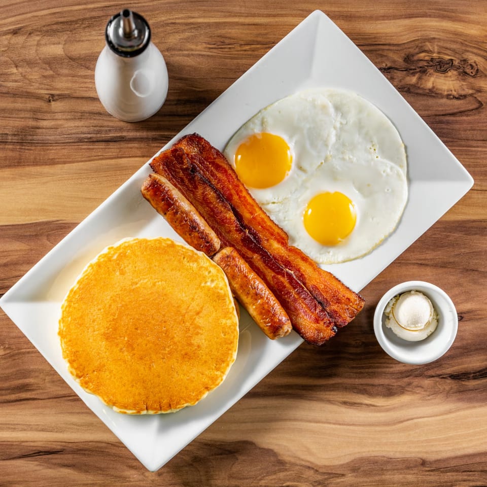 Buttermilk Eatery's breakfast platter with pancakes, bacon, sausage, and two fried eggs.