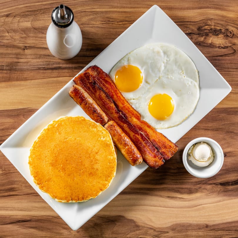 Buttermilk Eatery's breakfast platter with pancakes, bacon, sausage, and two fried eggs.