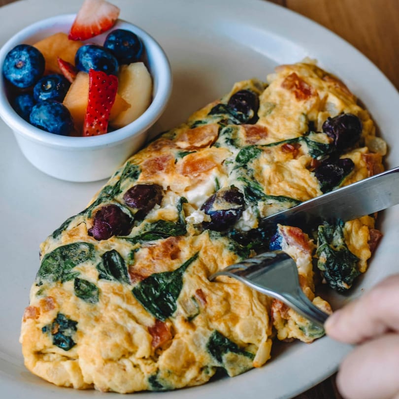 Buttermilk Eatery's omelet with spinach, olives, and tomatoes, served with a side of fresh fruit.