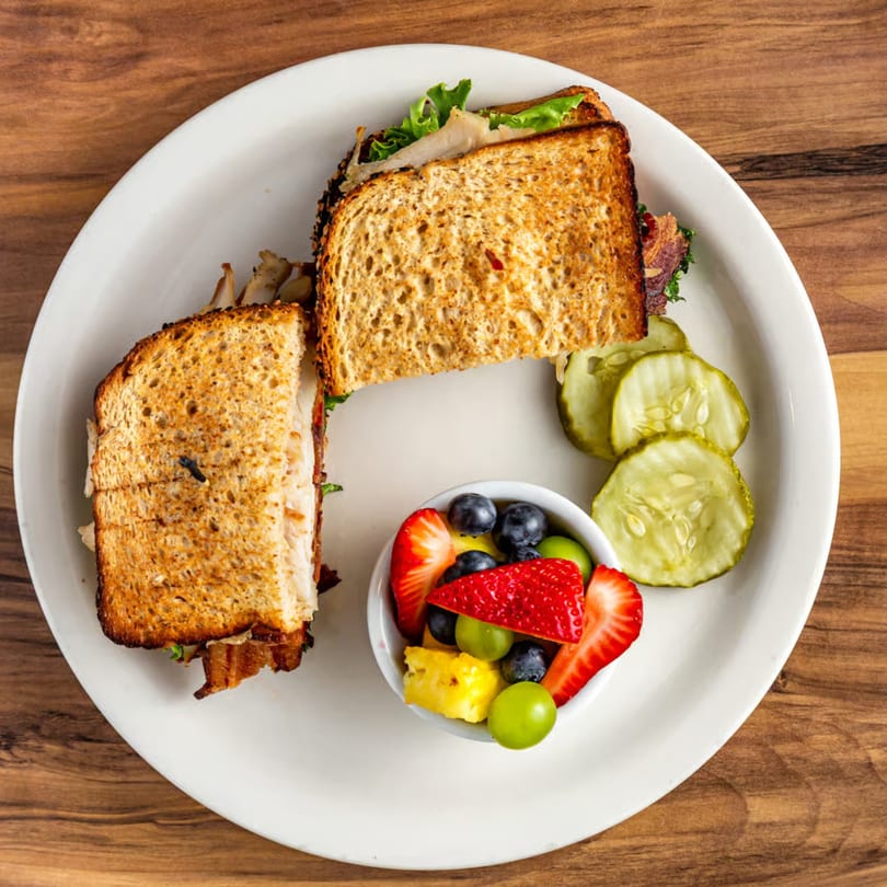 Buttermilk Eatery's breakfast sandwich with toasted bread, side of fruit salad, and pickle slices.