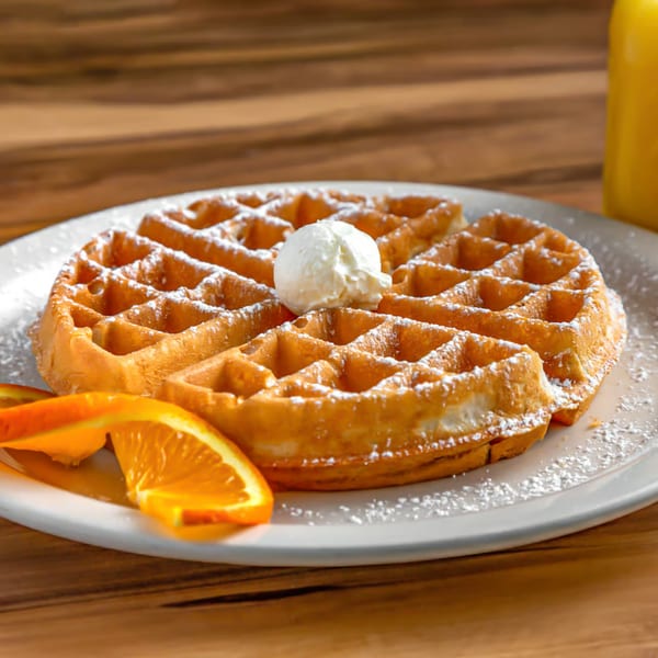 Buttermilk Eatery's golden waffle with powdered sugar, butter, and orange slices on a white plate.