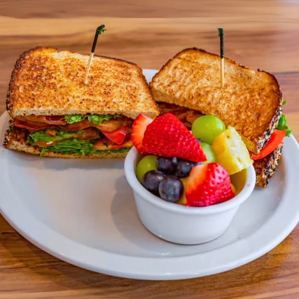 Toasted breakfast sandwich with lettuce, tomato, and bacon, served with a side of fresh fruit.
