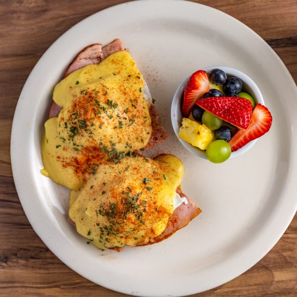 Buttermilk Eatery's Eggs Benedict with hollandaise sauce, paprika, and parsley, served with a fruit cup.