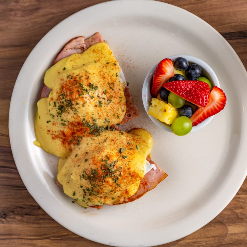 Buttermilk Eatery's Eggs Benedict with hollandaise sauce, paprika, and parsley, served with a fruit cup.