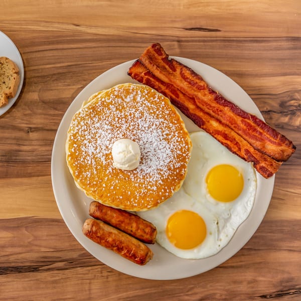 Buttermilk Eatery's breakfast plate with pancakes, bacon, sausage links, and two fried eggs.