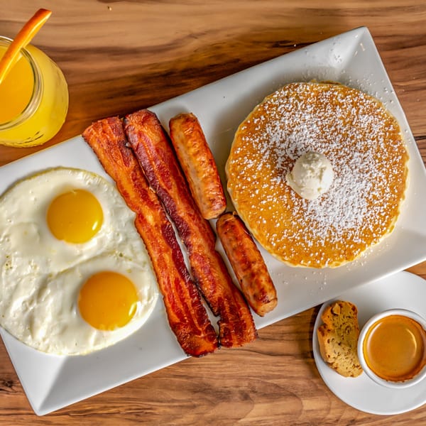 Buttermilk Eatery's breakfast platter with pancakes, bacon, sausage, fried eggs, orange juice, and espresso.