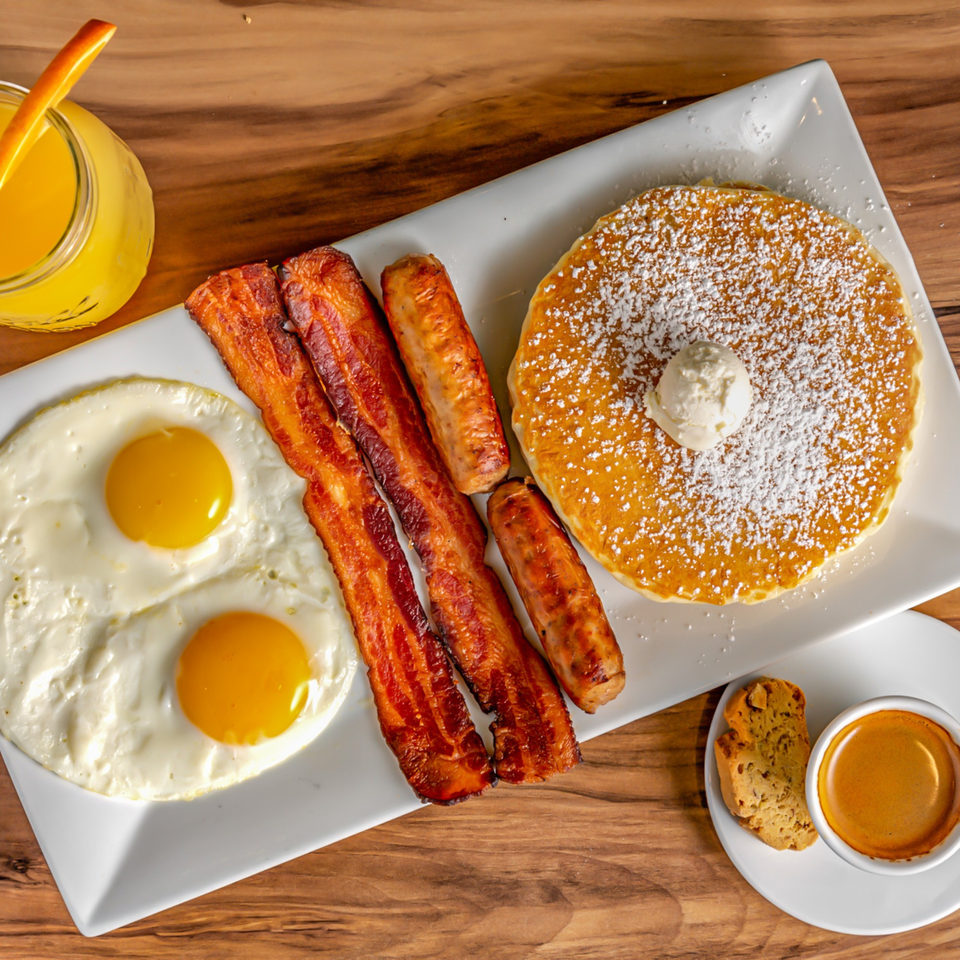 Buttermilk Eatery's breakfast platter with pancakes, bacon, sausage, fried eggs, orange juice, and espresso.